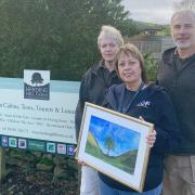 Helen Foster, centre, presents her painting of Sycamore Gap to Herding Hill Farm Camping and Glamping Site managers Phil and Sue Humphreys